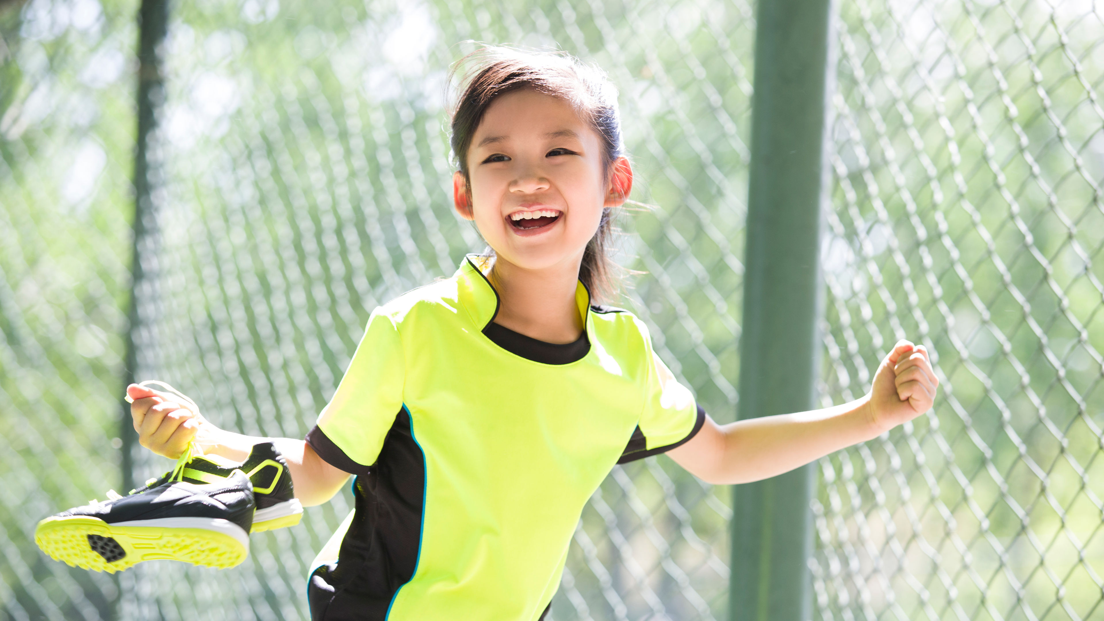 A happy girl in yellow sportswear, holding a pair of shoes in her hands.