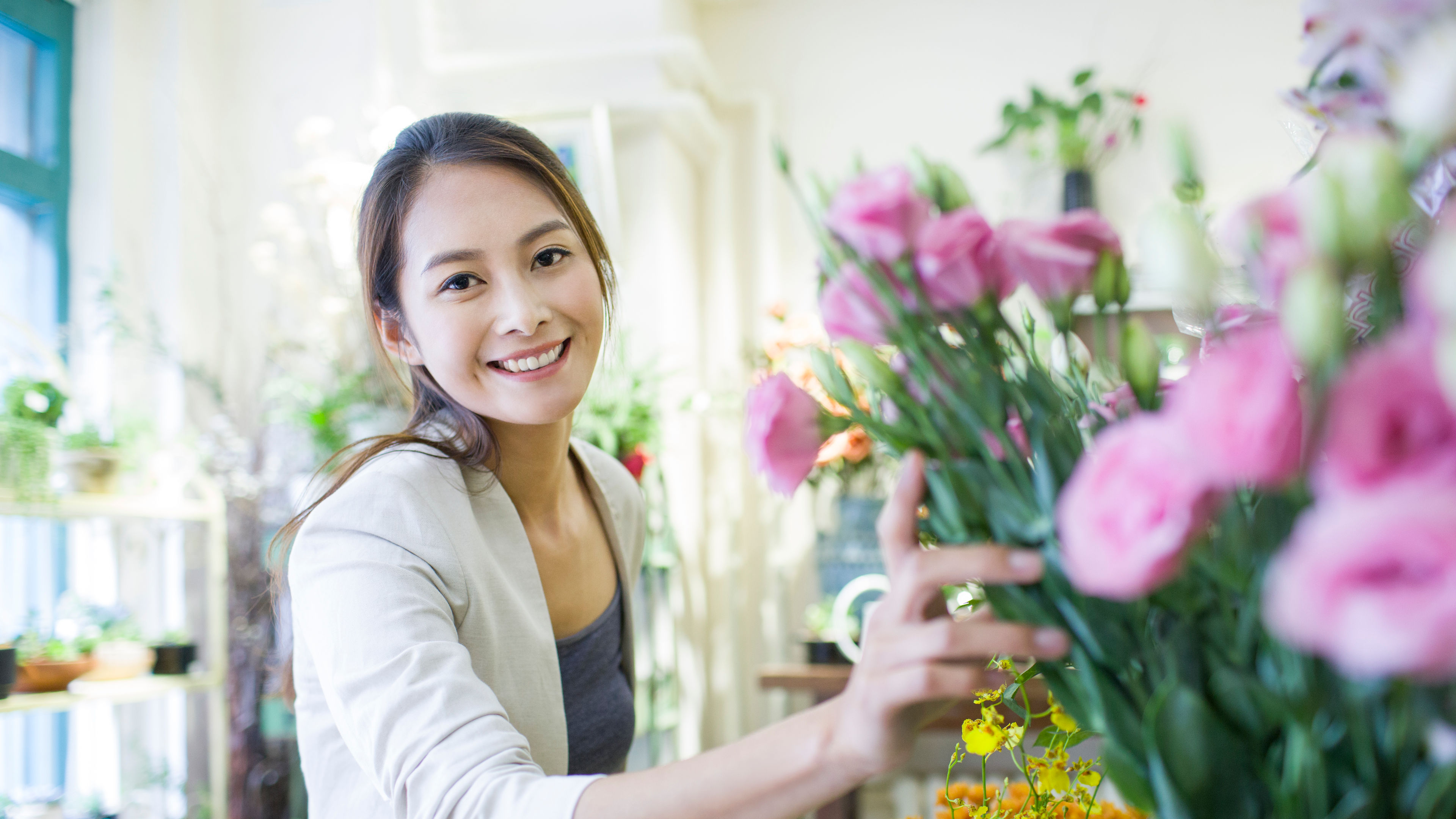 A pretty woman standing inside a flower shop, holding a bouquet of flowers in her hands with a bright smile.