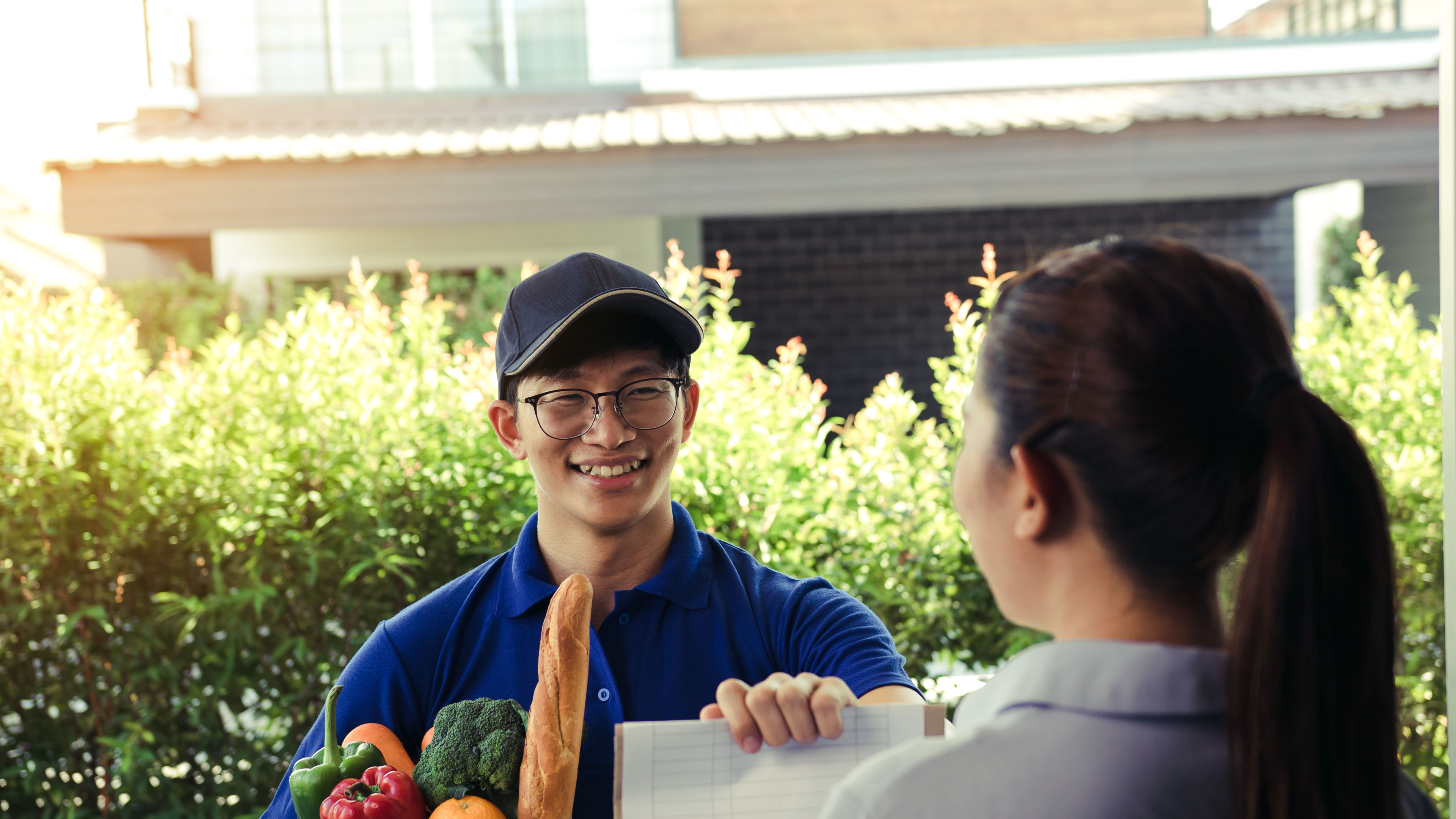 Supermarket food delivery staff deliver bags to female customers in front of the house. 