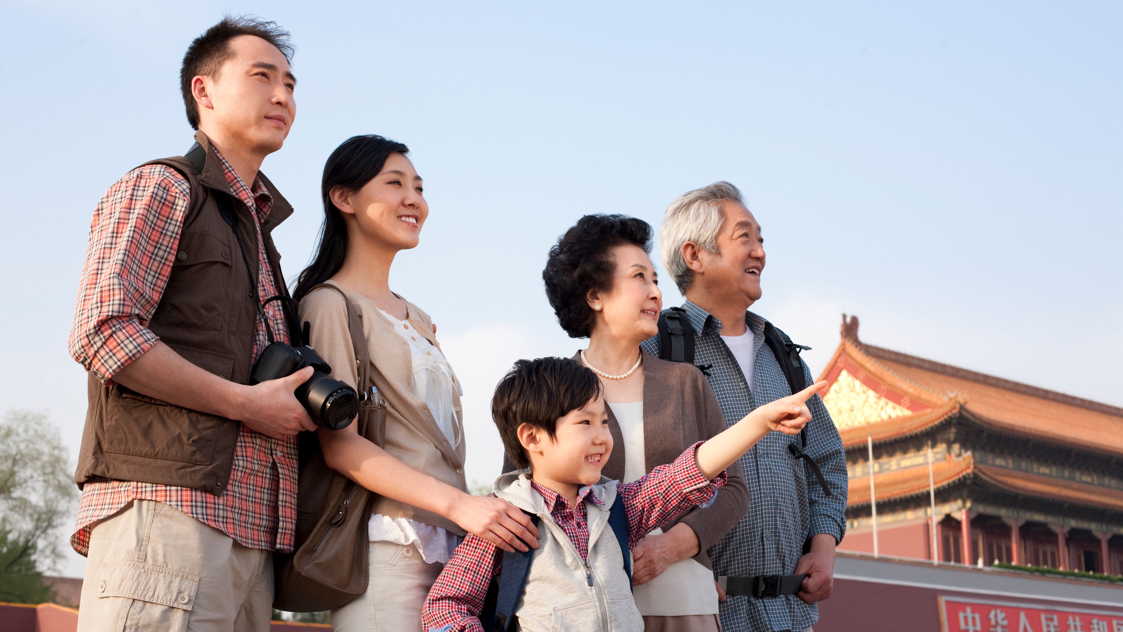 A joyful multi-generational family stands together at Tiananmen Square, the child pointing excitedly 