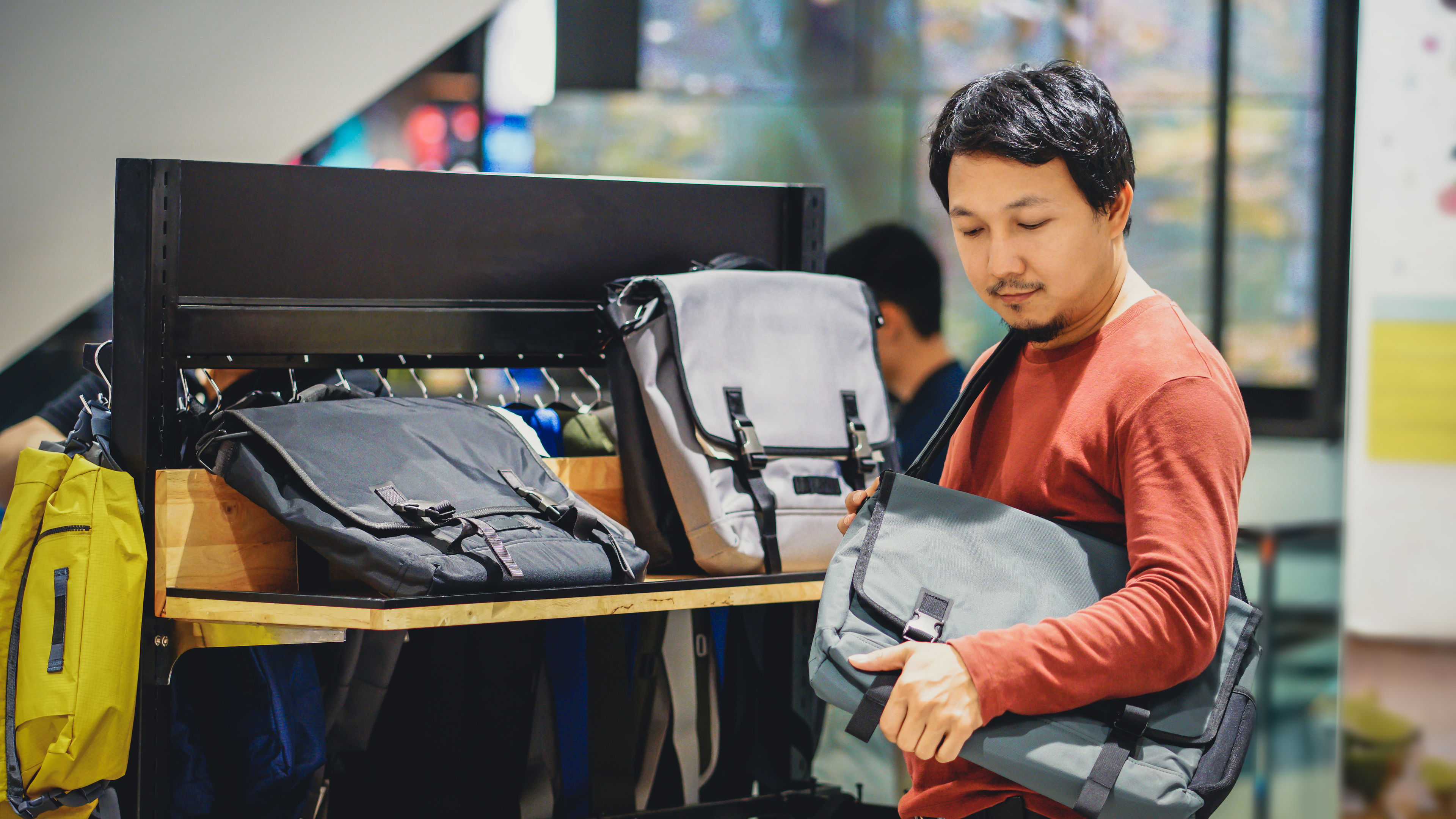 A man with a beard trying bags and making decisions in a fashion bag shop at a shopping mall. 