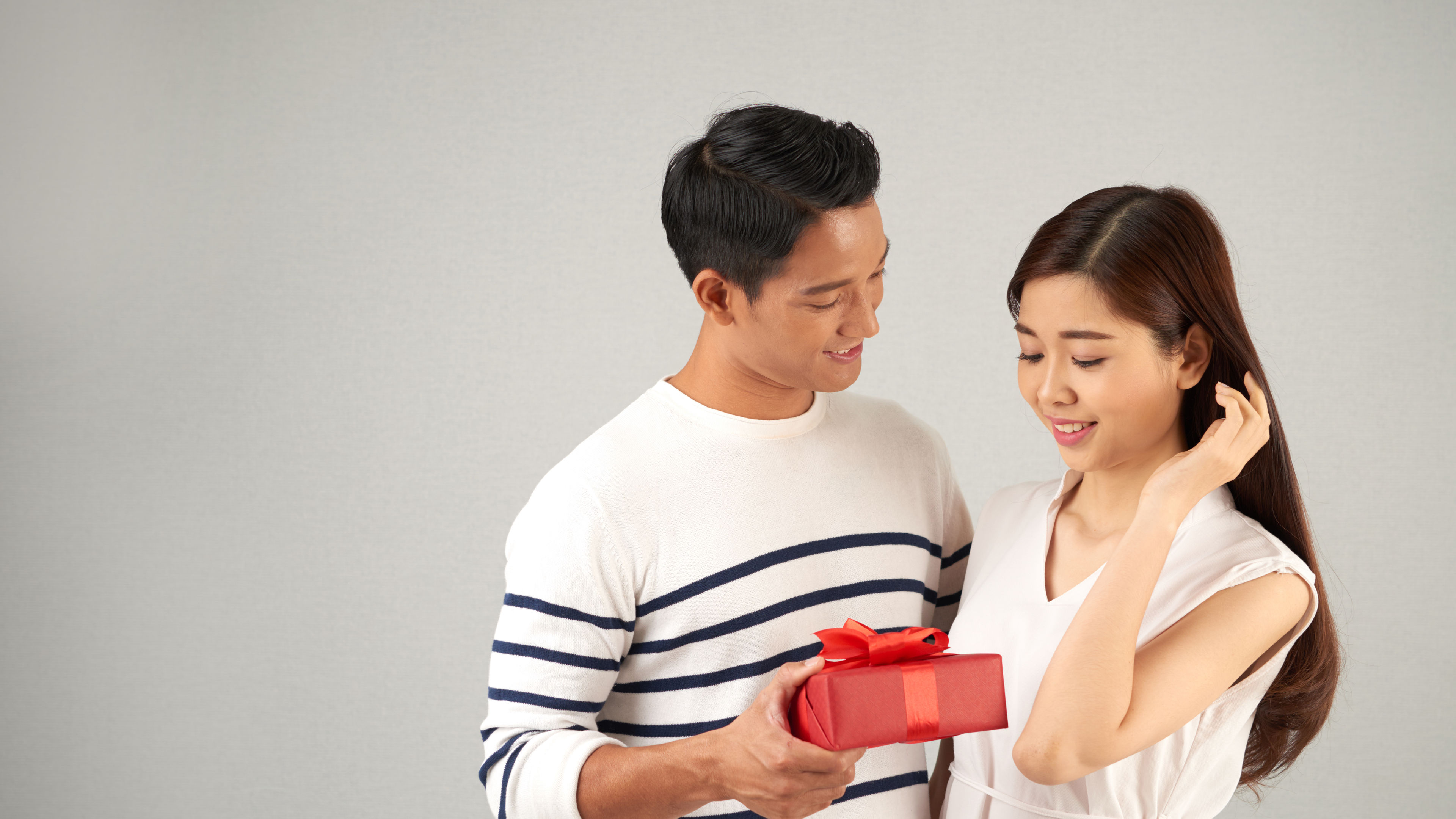 A cheerful man presents a beautifully wrapped red gift box to a smiling woman 