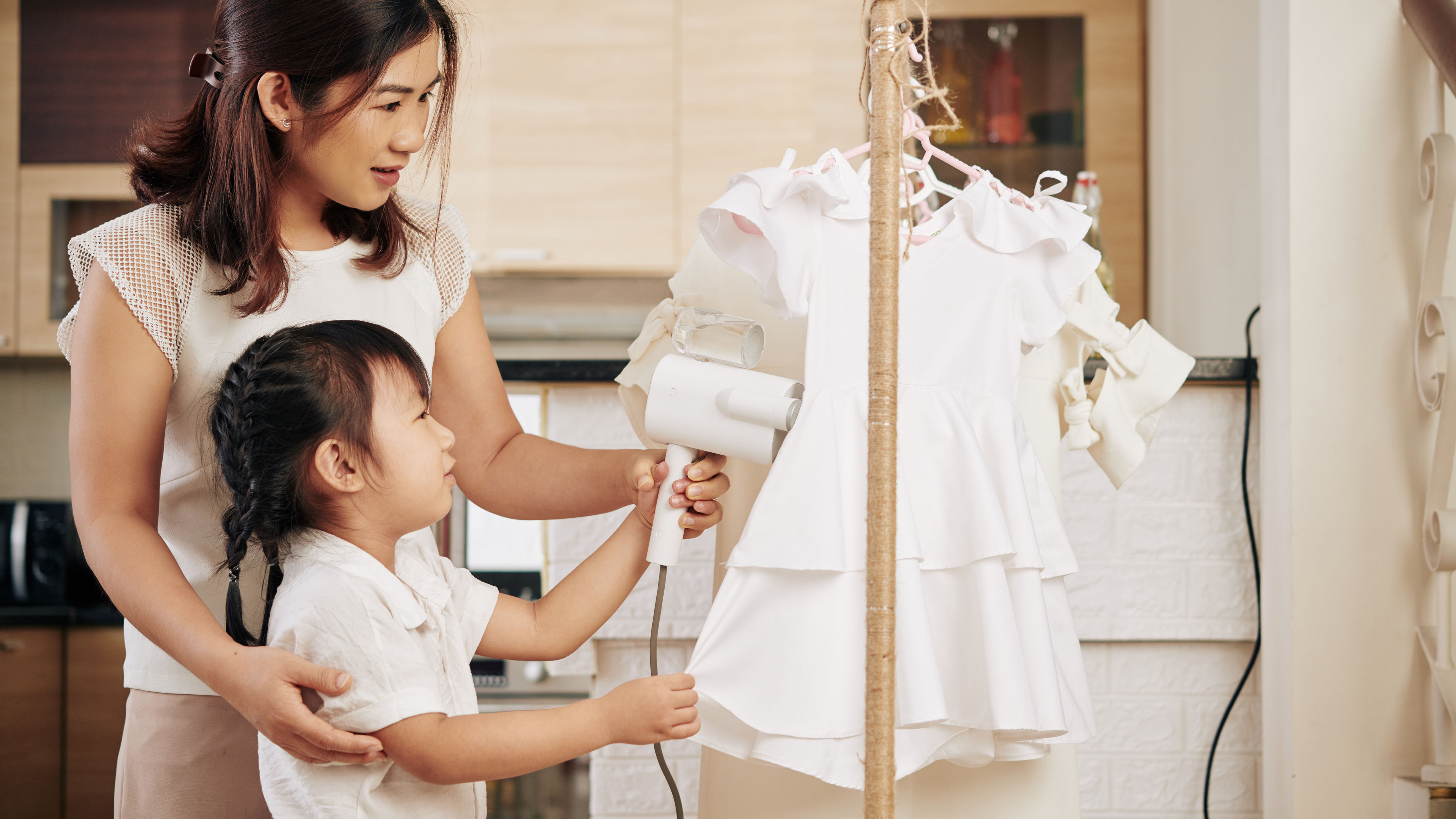 A mother helps her child steam a dress. 
