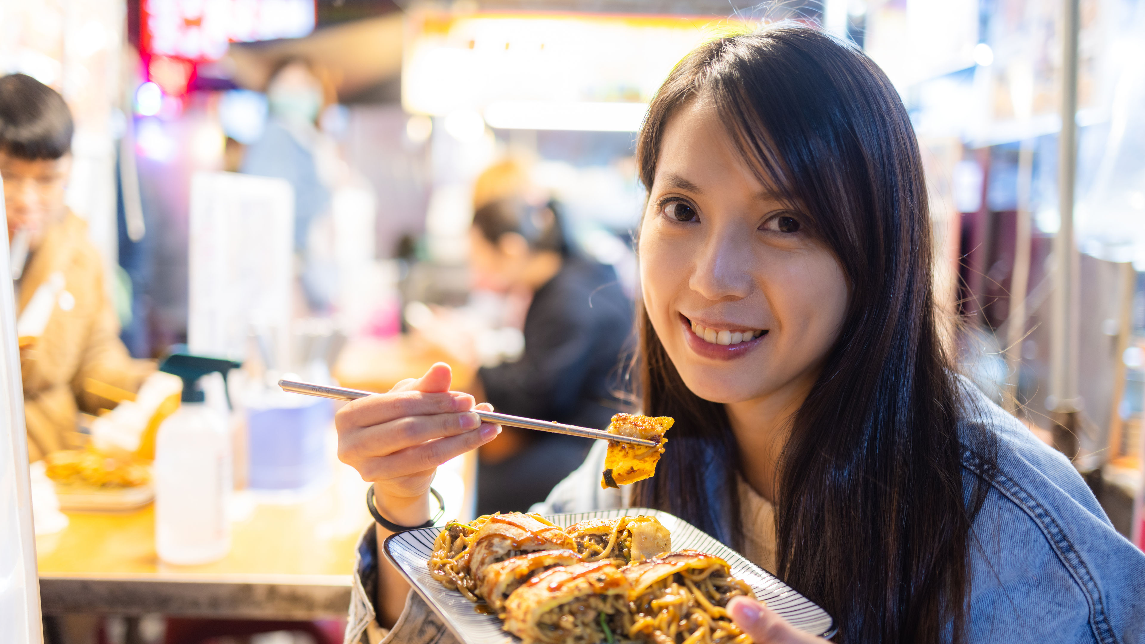 A smiling woman enjoys a delicious plate of pan-fried noodles  