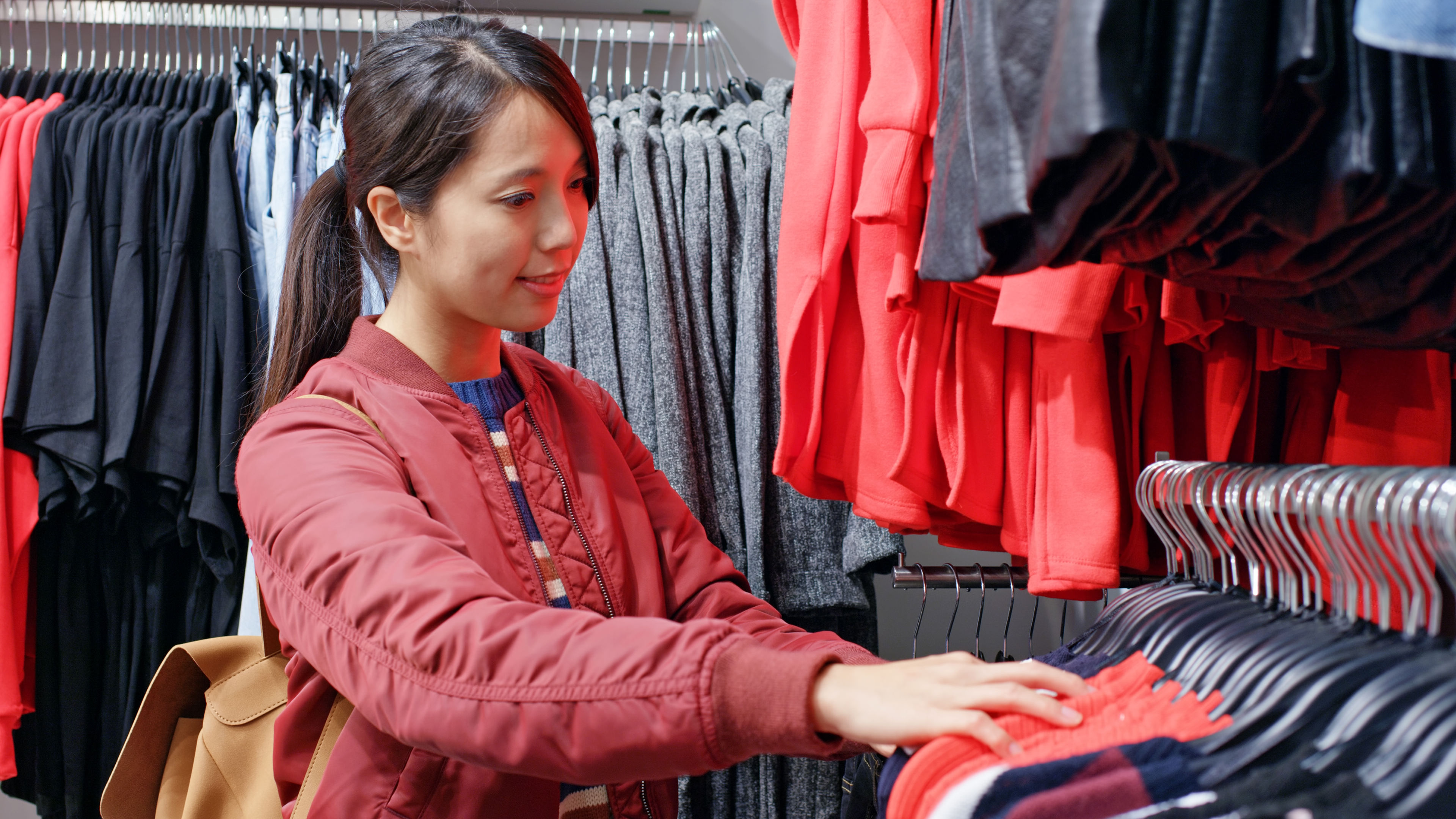 A cheerful shopper explores a collection of bright red tops in a fashion boutique 
