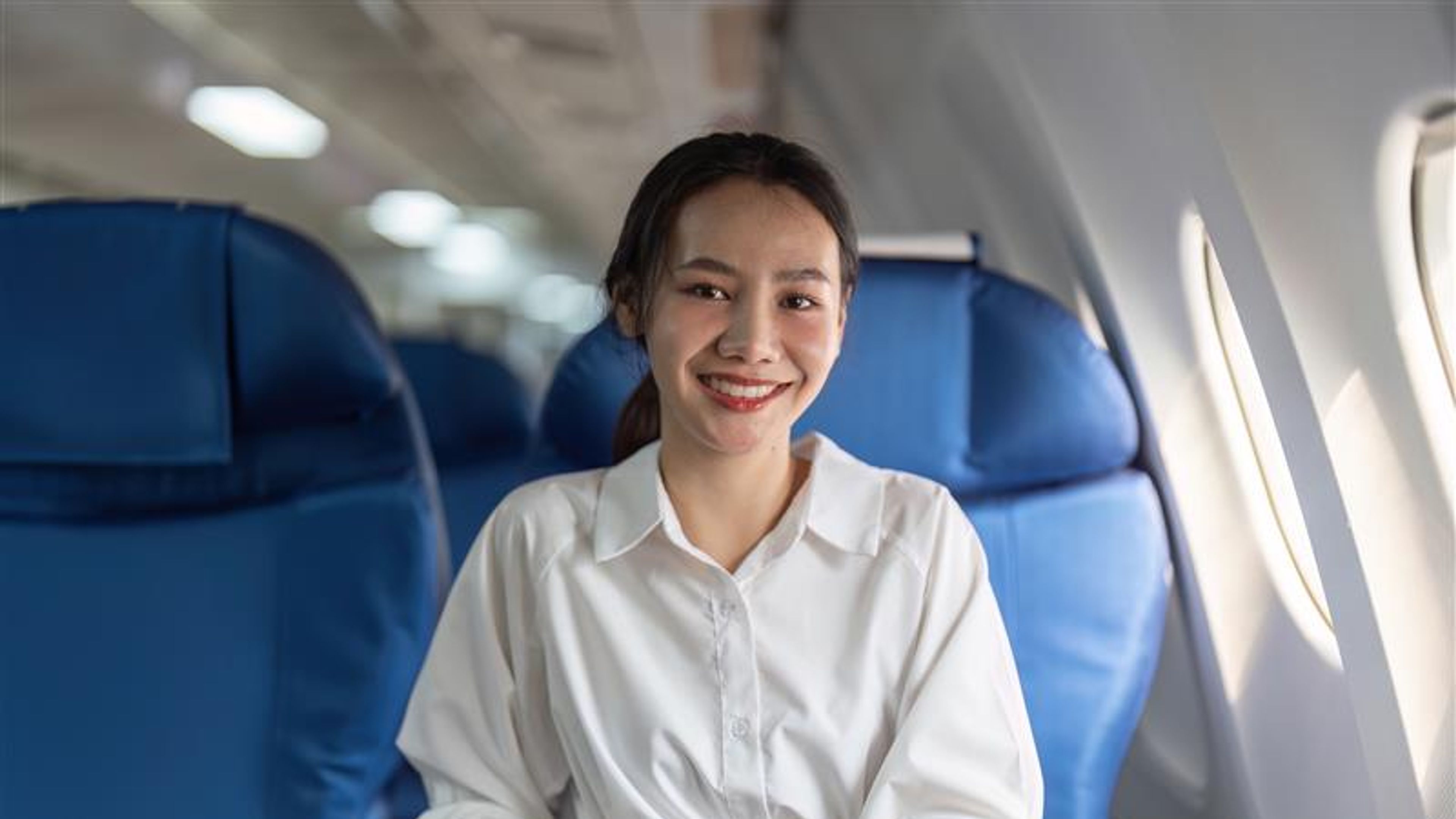 A woman is sitting on a blue airplane seat with a smile on her face. 