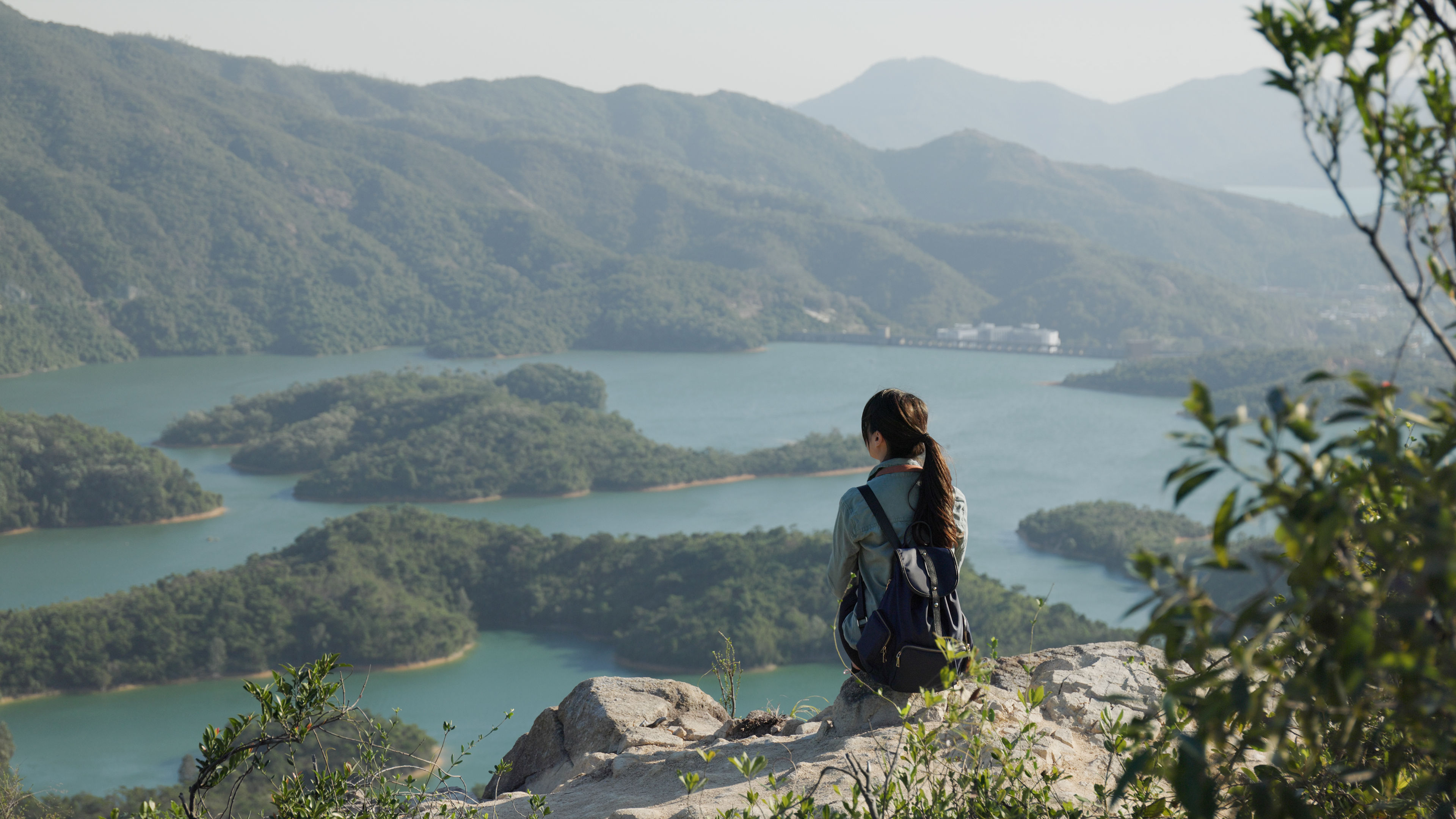 A Woman sits on the top of the mountain and looks at the scenery view 