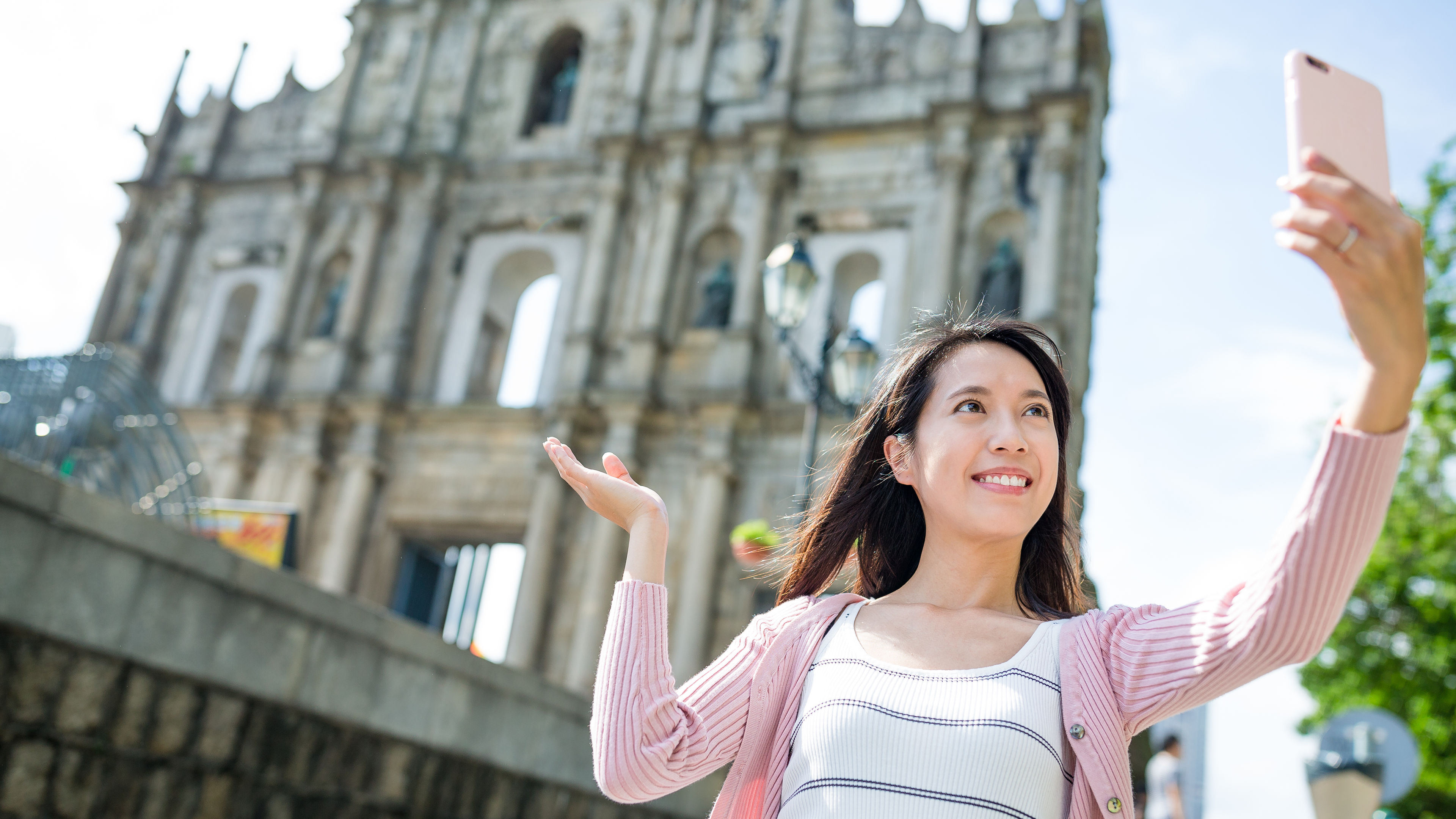 A woman taking a selfie in Macau city with a church in the backside. 