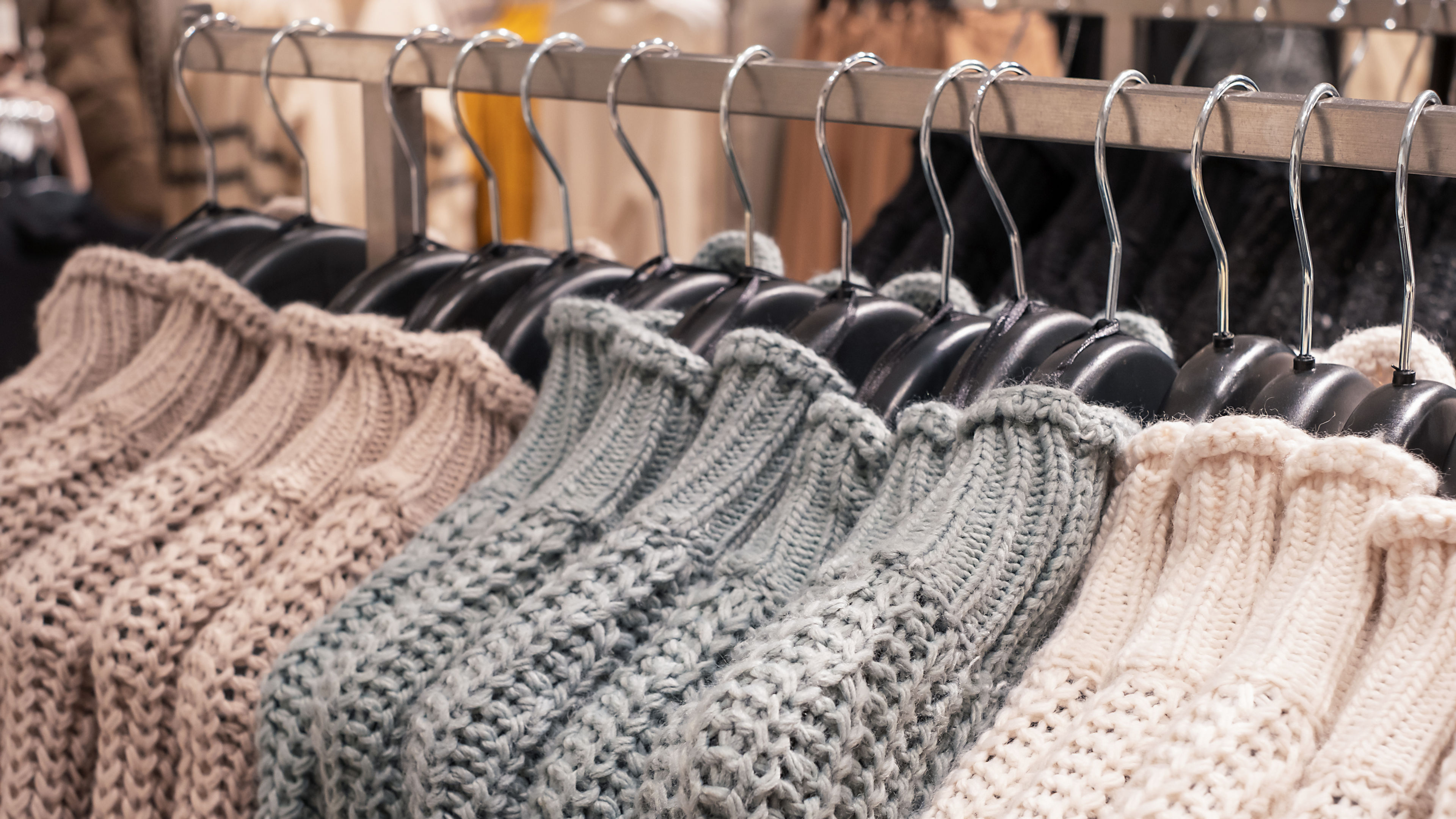 A collection of soft, knitted sweaters in earthy tones and pastel shades hangs neatly on black hangers 