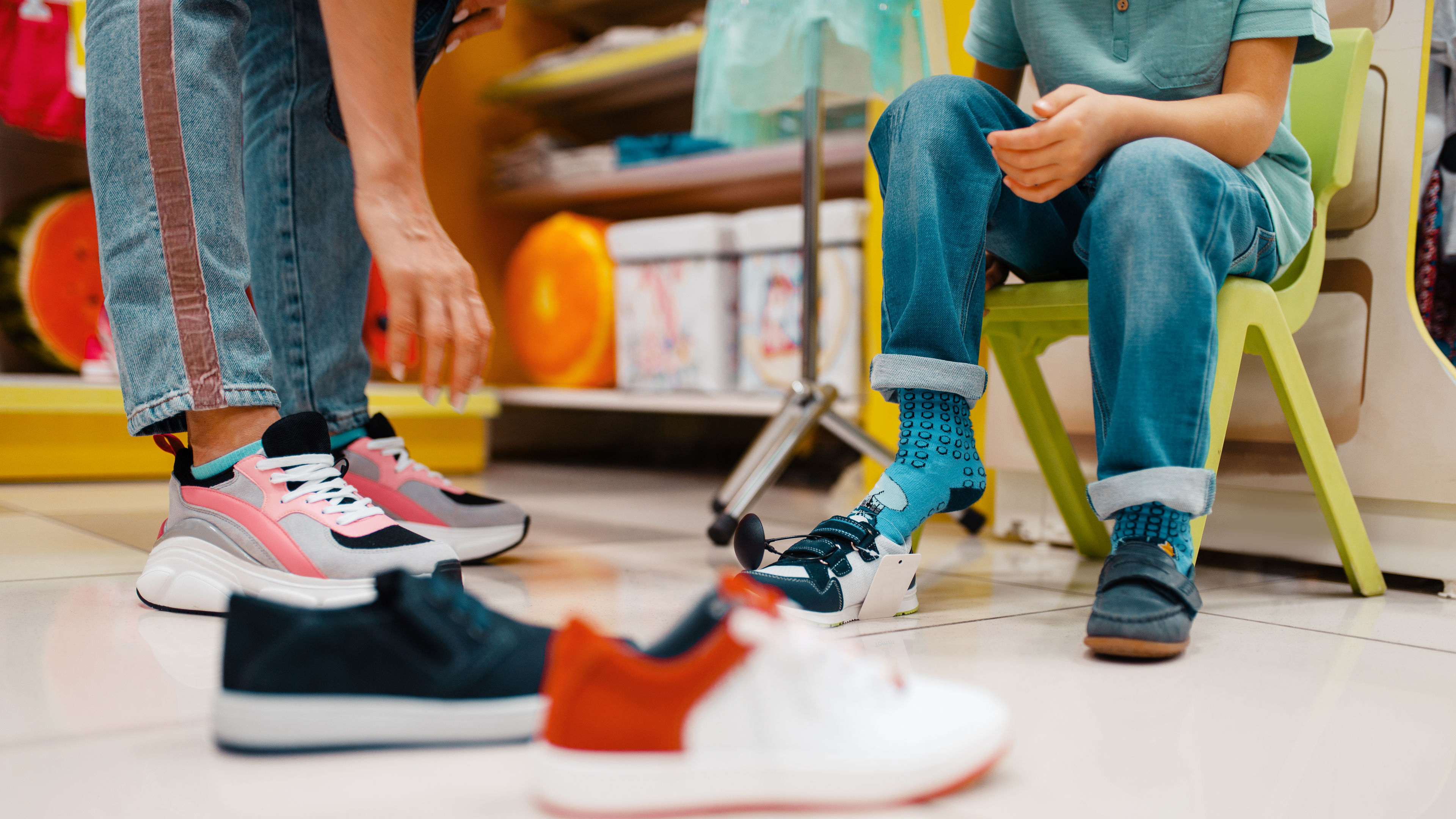 A child is trying on shoes in a store with the help of his mother 
