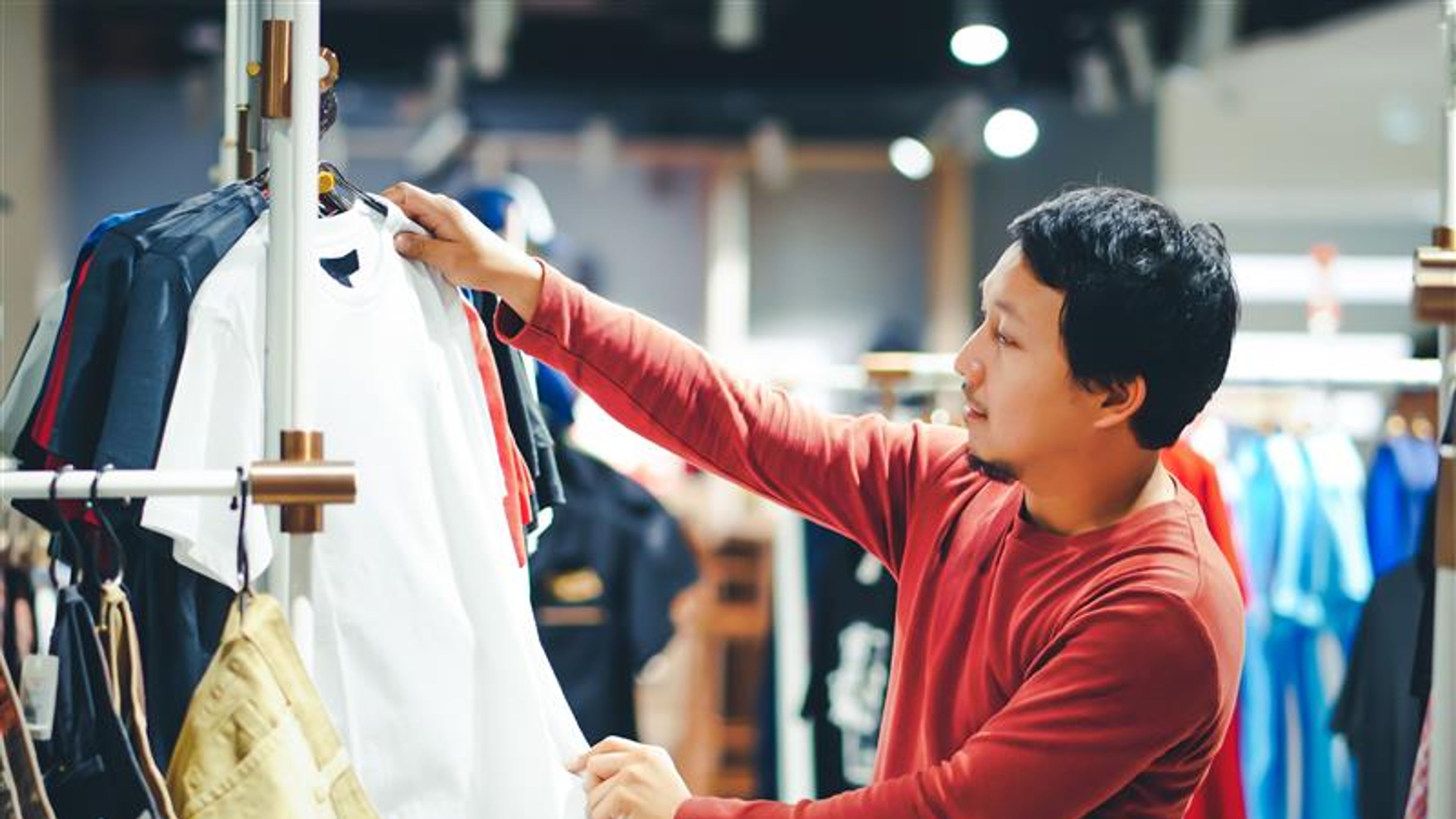Smart man with beard choosing clothes in clothing store at shopping centre