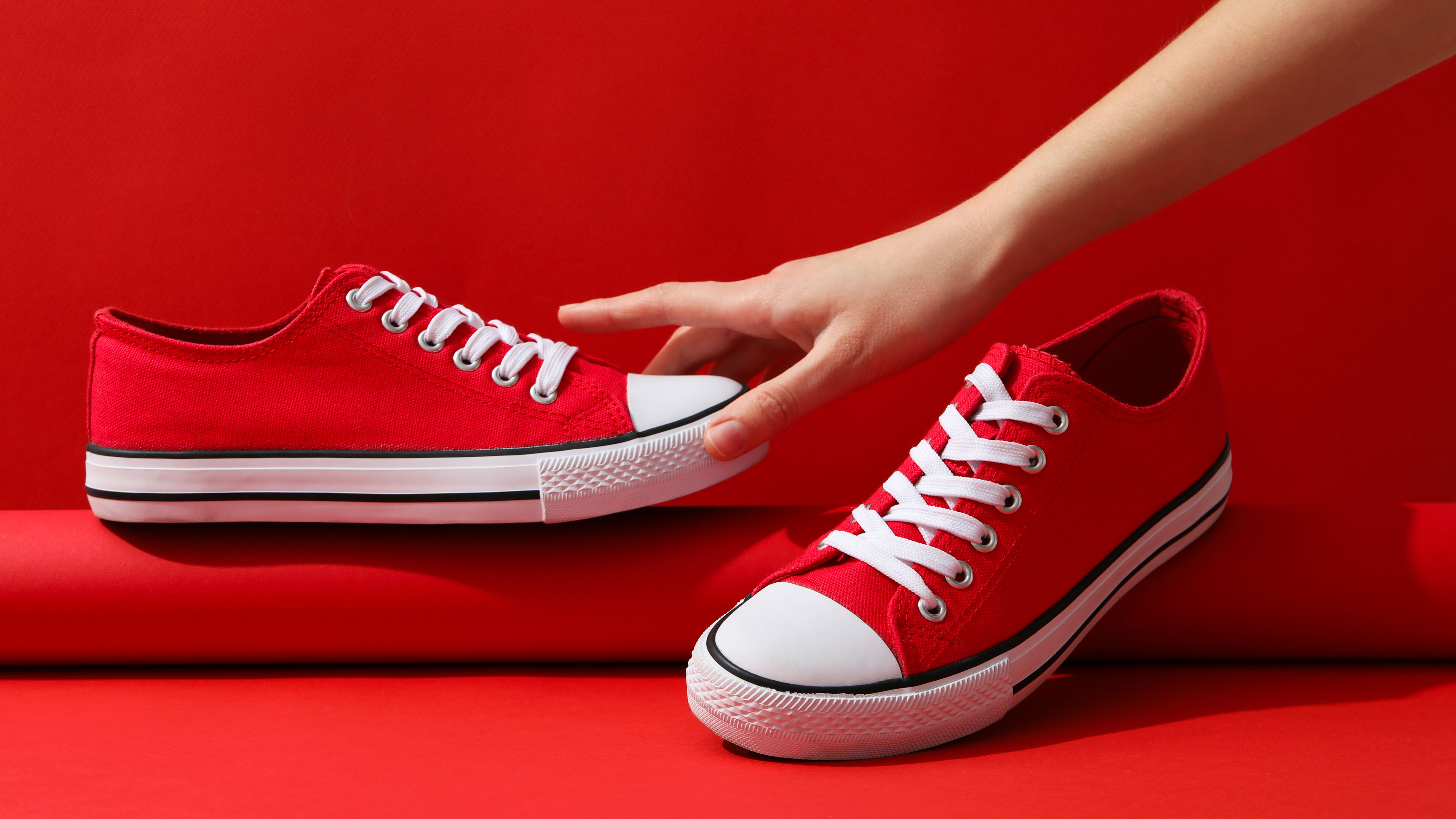 A pair of vibrant red sneakers is displayed on a red background 
