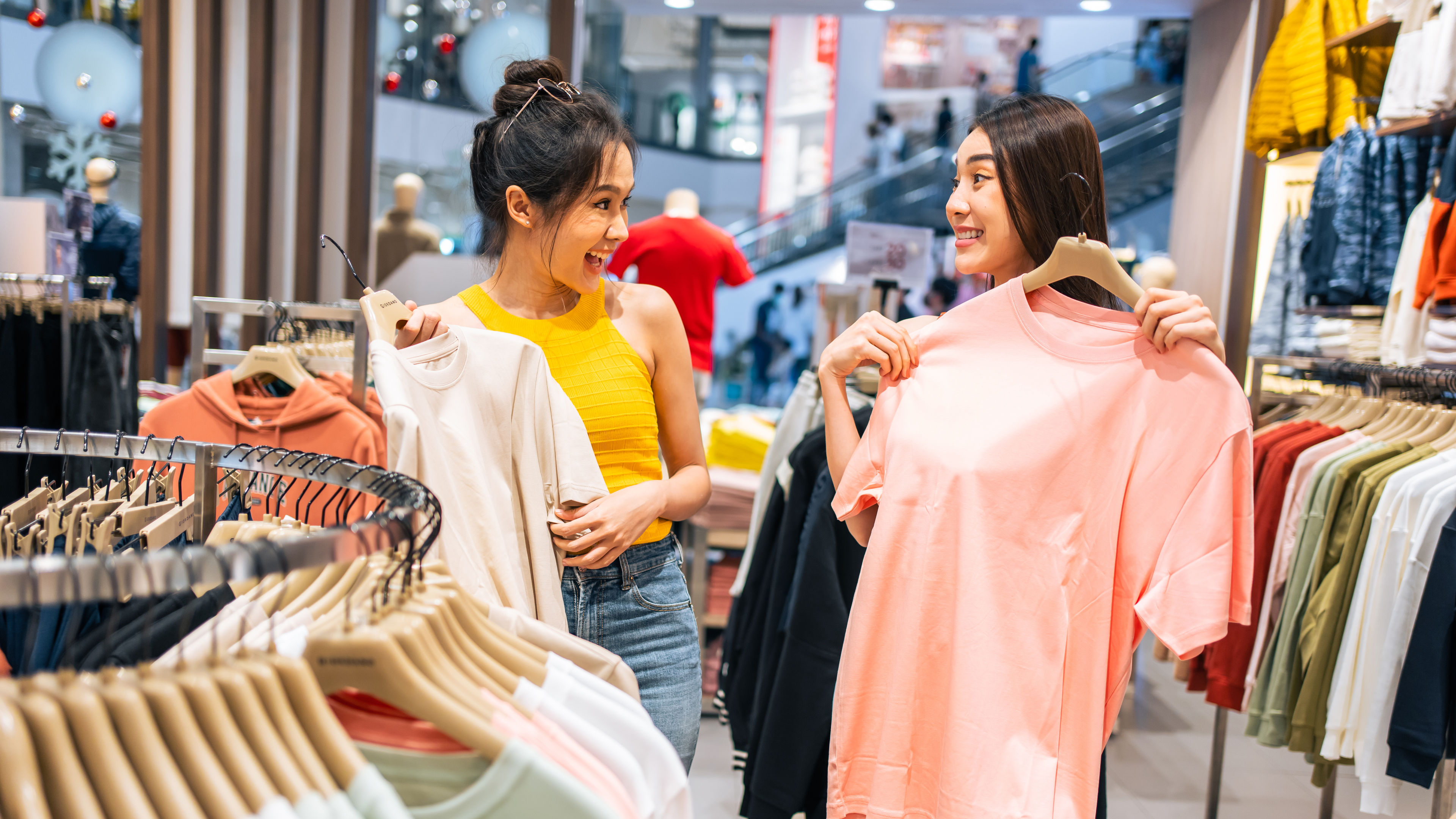 Two Asian women holding vibrant red and gold dresses, symbolising prosperity and festive elegance for Chinese New Year. 