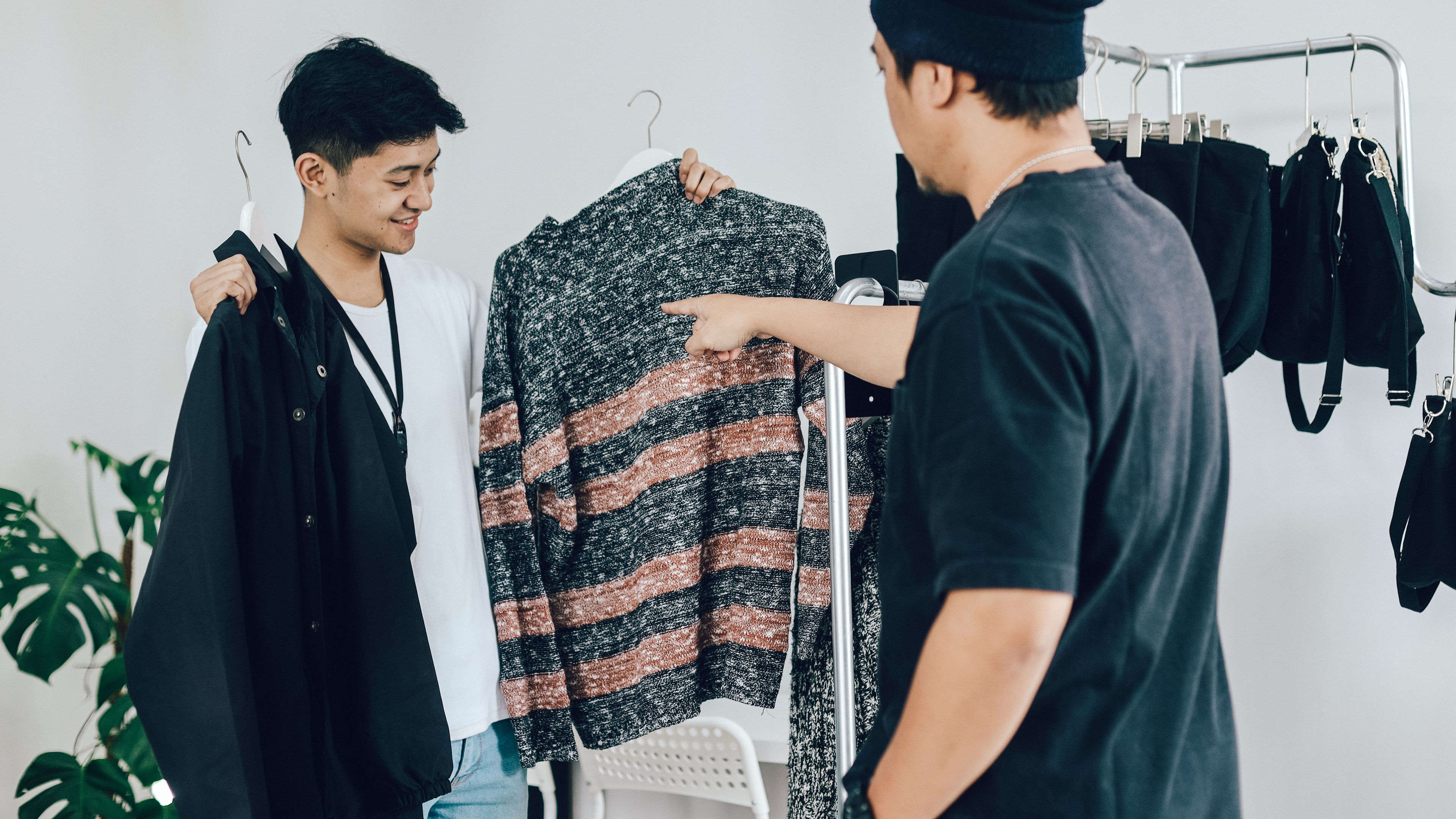 Two young men enthusiastically discuss a striped sweater while browsing a clothing rack 