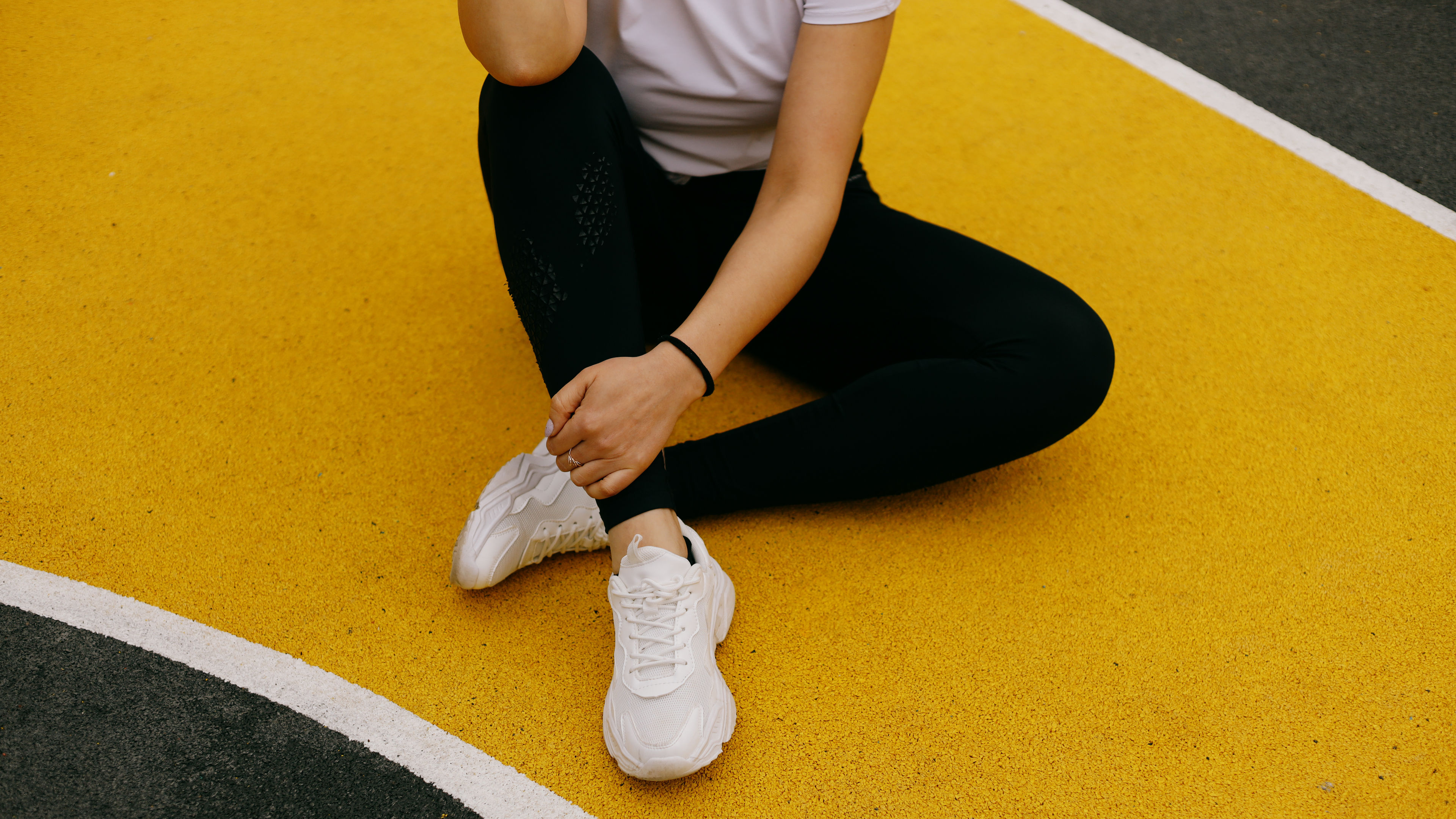 A person is sitting on a yellow and black court wearing white sneakers and black leggings, 
