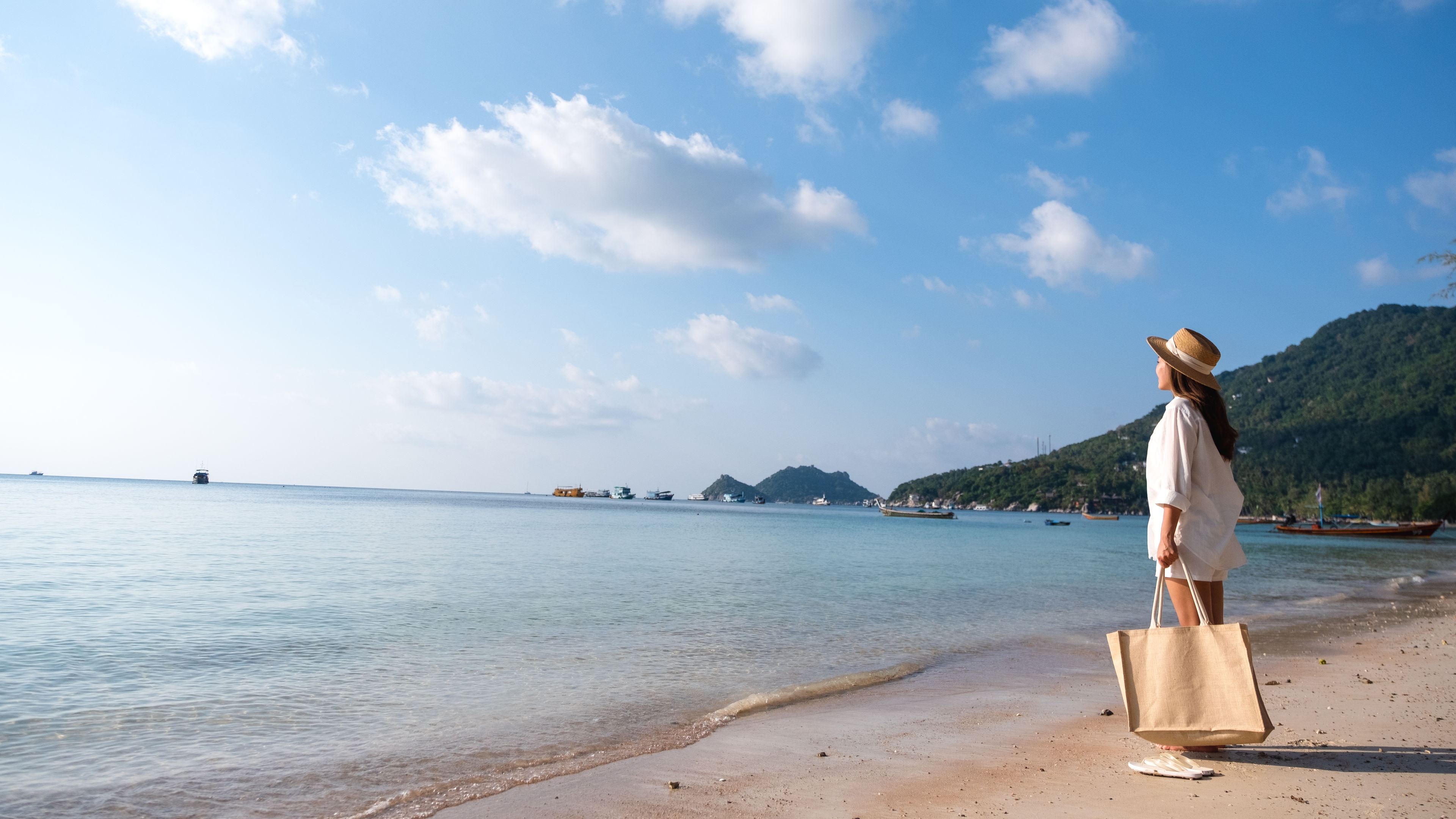 Portrait image of a beautiful young asian woman with hat and bag strolling on the beach 