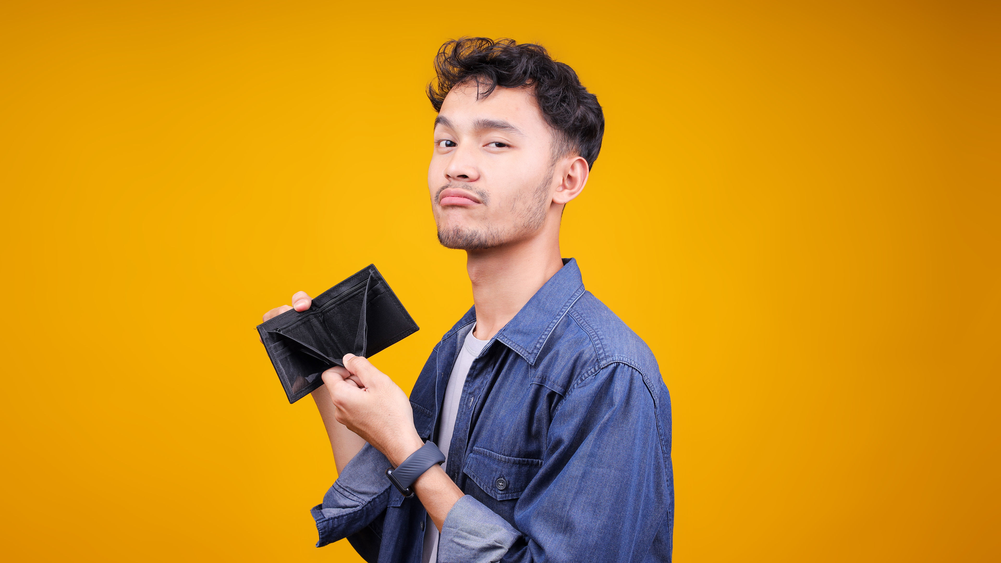 Young man feeling sad while showing empty wallet over yellow Background
